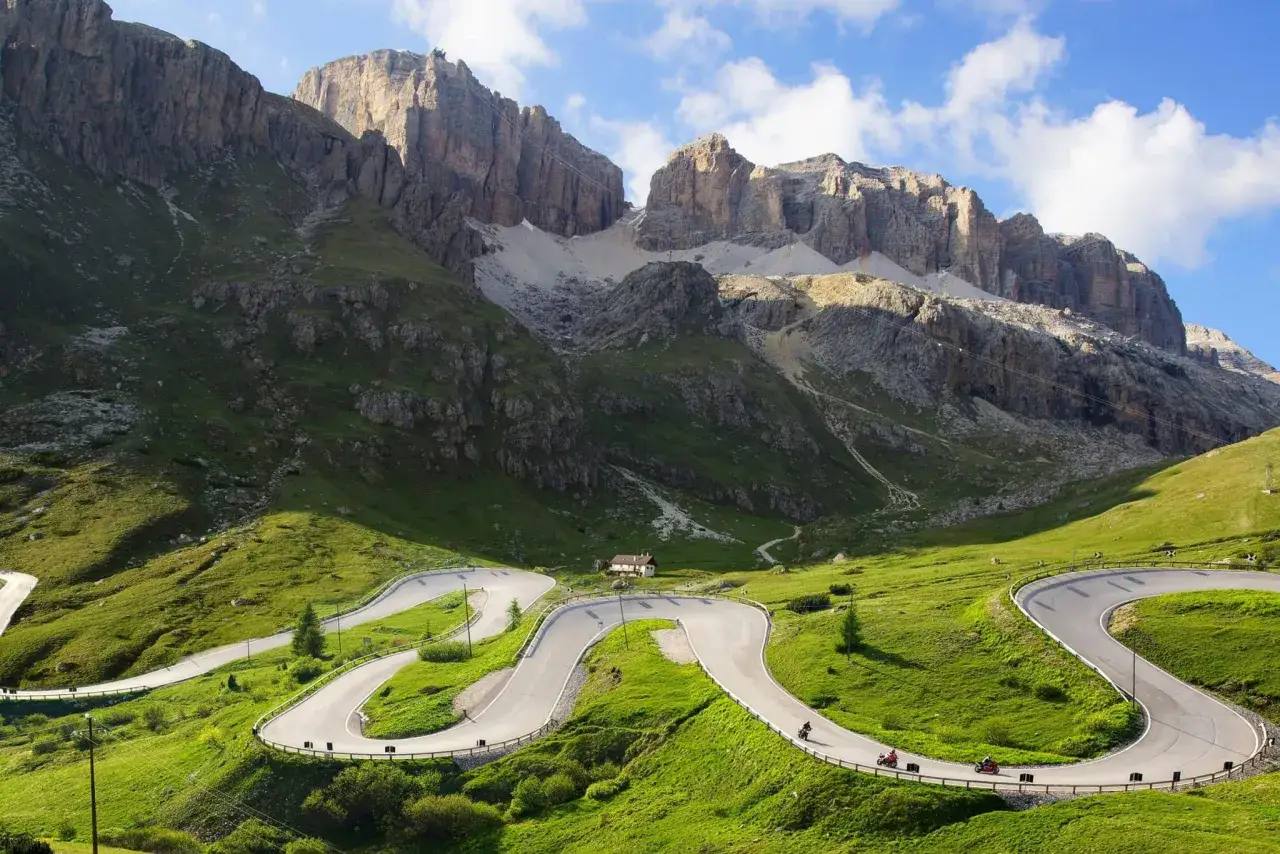 Motorcyclists enjoy a scenic **Italy bike tour** on a winding mountain road through the Dolomites, with dramatic peaks under a blue sky.