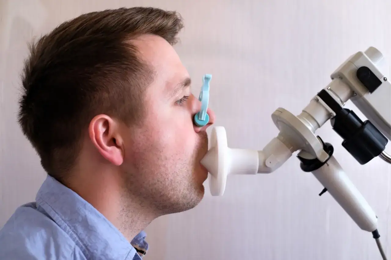 Mężczyzna wykonuje badanie spirometria, z klipsem na nosie i ustnikiem urządzenia.