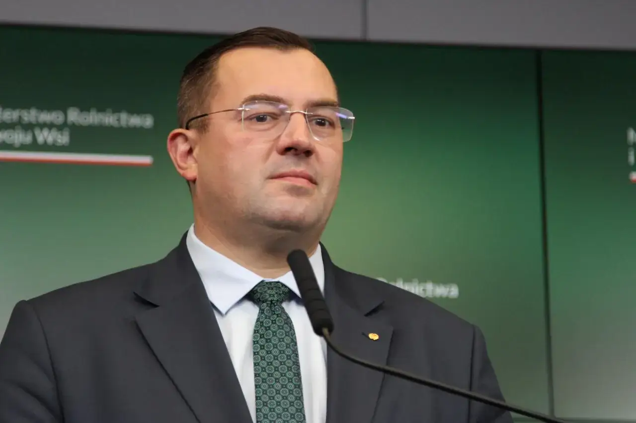 Minister rolnictwa w garniturze i krawacie przed mikrofonem.