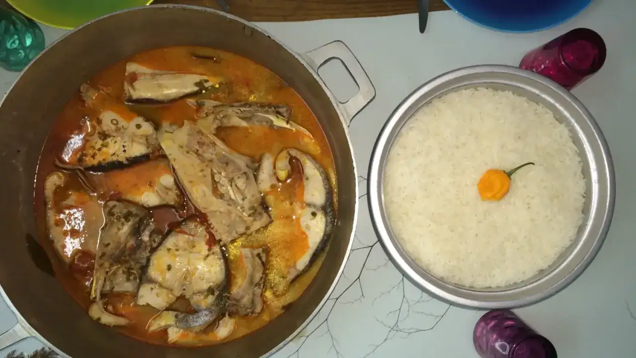 Poisson en cuisson court bouillon dans une marmite, accompagné d'un bol de riz blanc orné d'un piment jaune.
