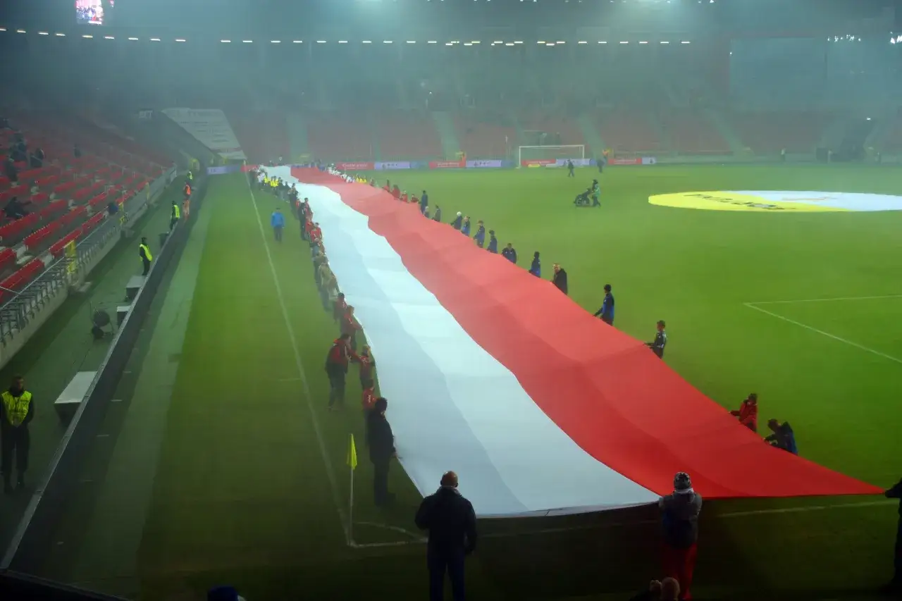 Piłkarze GKS Tychy i Odry Opole rozwijają ogromną flagę Polski na murawie stadionu.