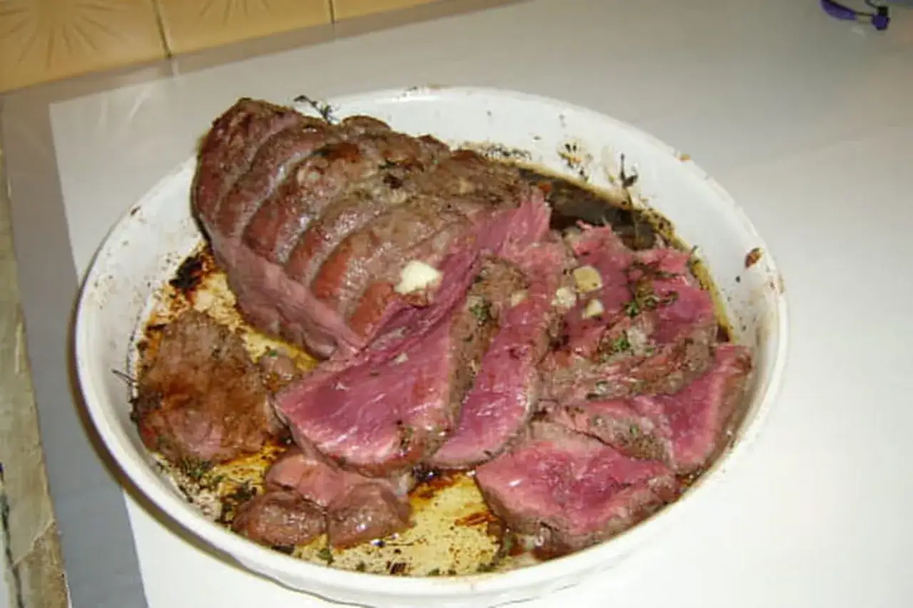 Un délicieux roti de boeuf, tranché et servi dans un plat blanc, avec des herbes et de l'ail.