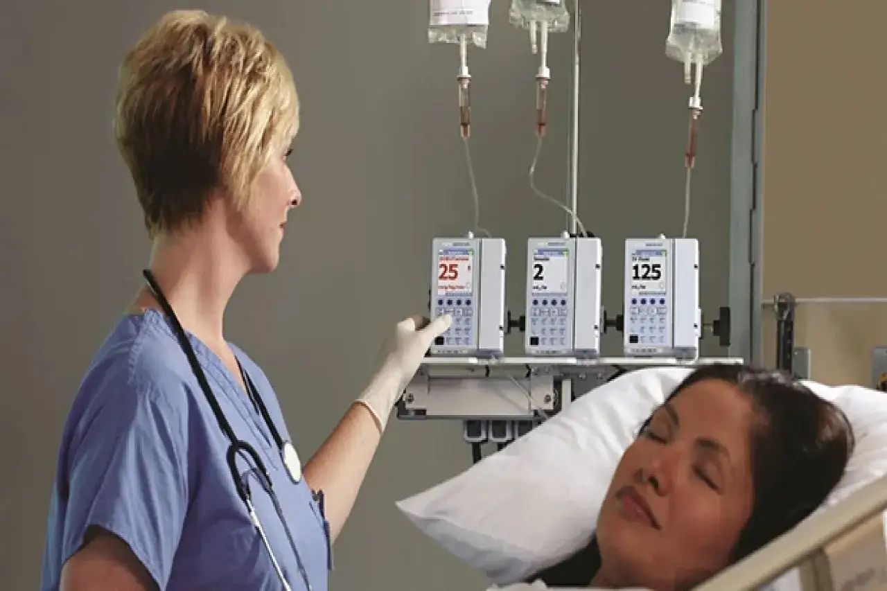 Pielęgniarka ustawia pompy infuzyjne, przygotowując kropl&oacute;wkę. Pacjentka leży w ł&oacute;żku.