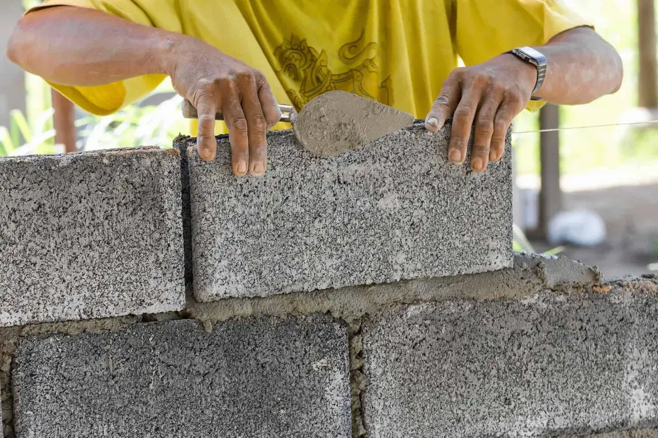 Budowniczy układa bloczek na świeżej zaprawie, tworząc ścianę fundamentową z bloczków betonowych.