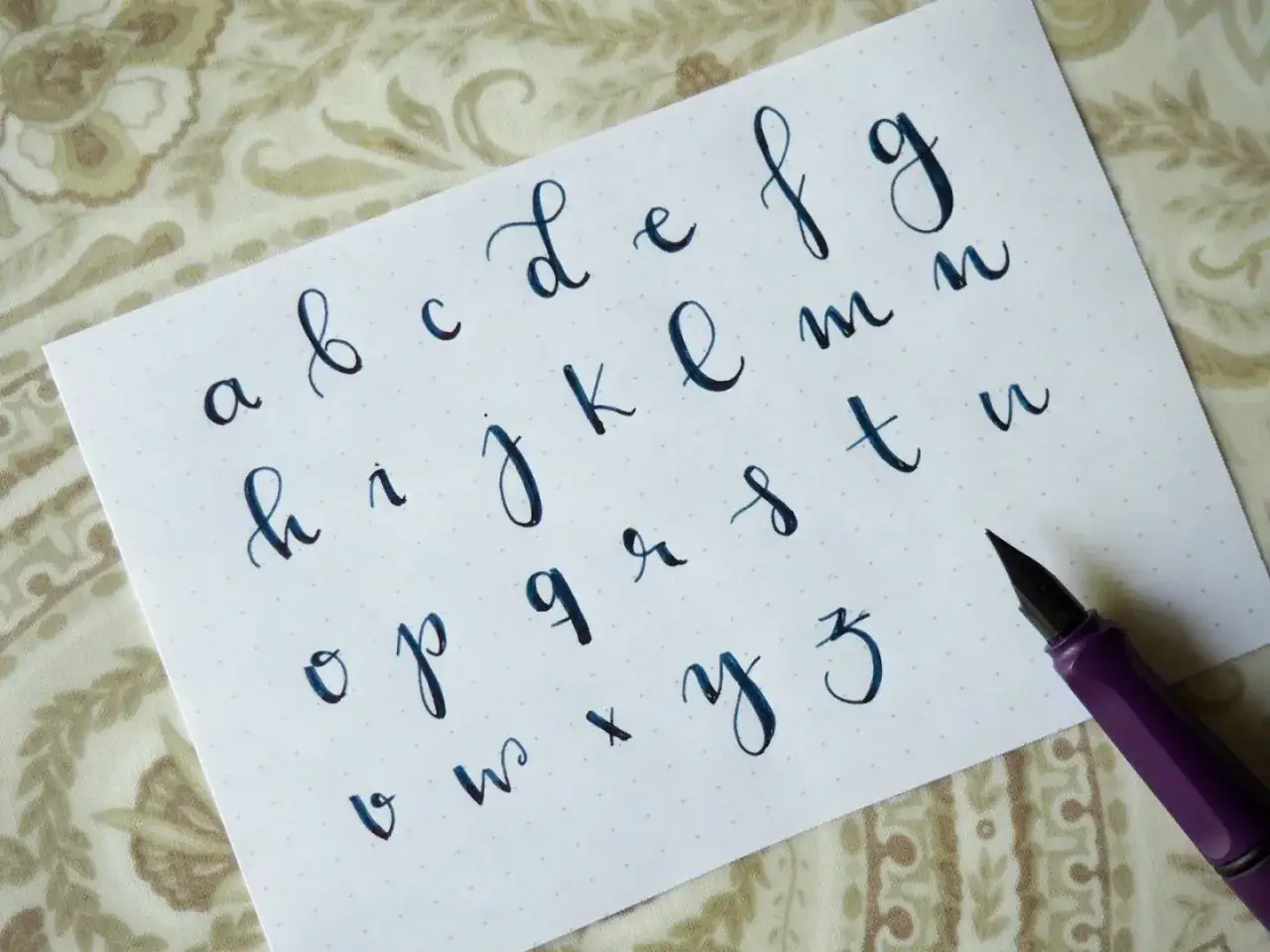Un abecedario con lettering bonito en cursiva azul. Se aprecian las letras de la a a la z, escritas con una pluma morada.