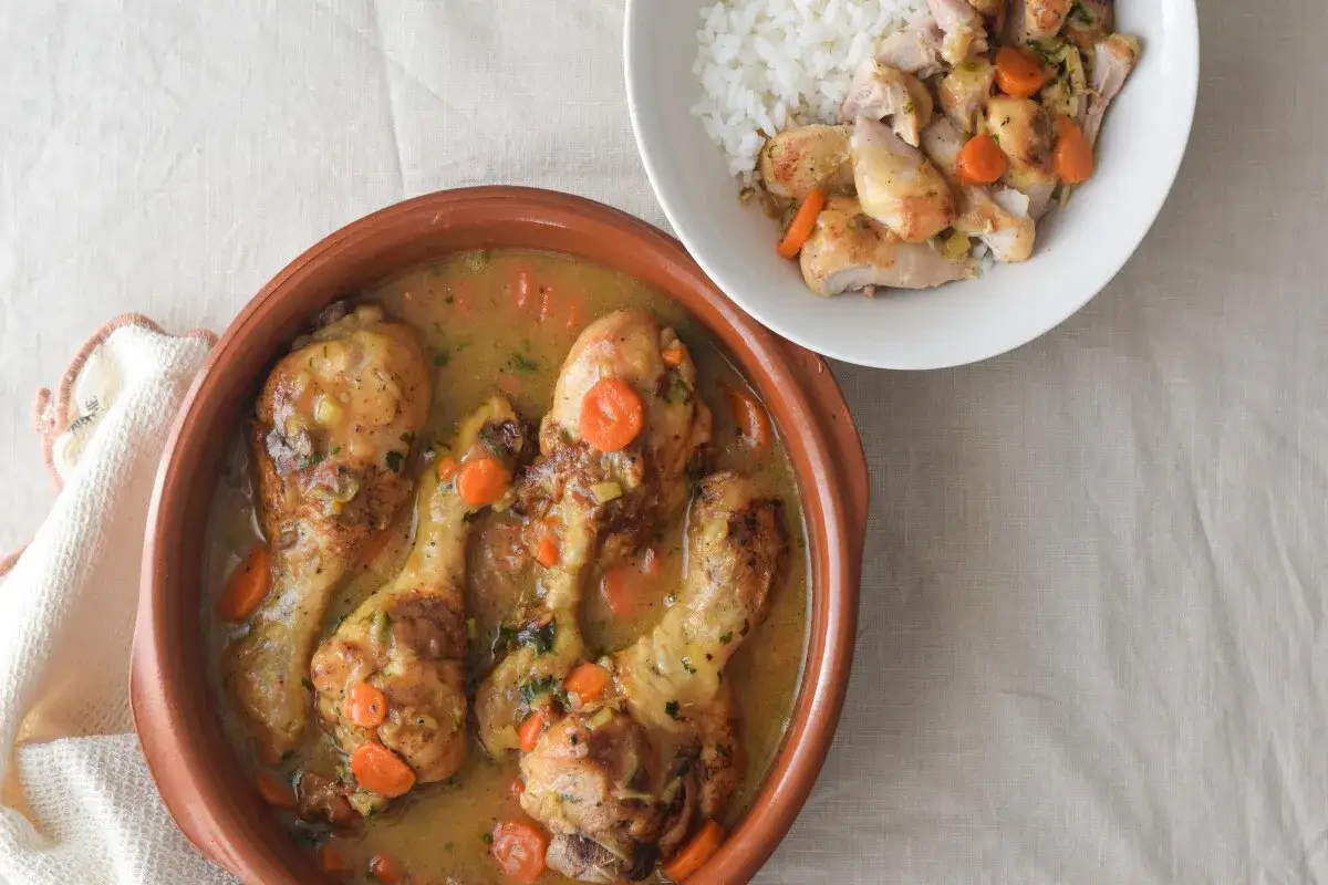 Jamoncitos de pollo guisados en una cazuela de barro con zanahorias y hierbas, acompañados de arroz blanco.