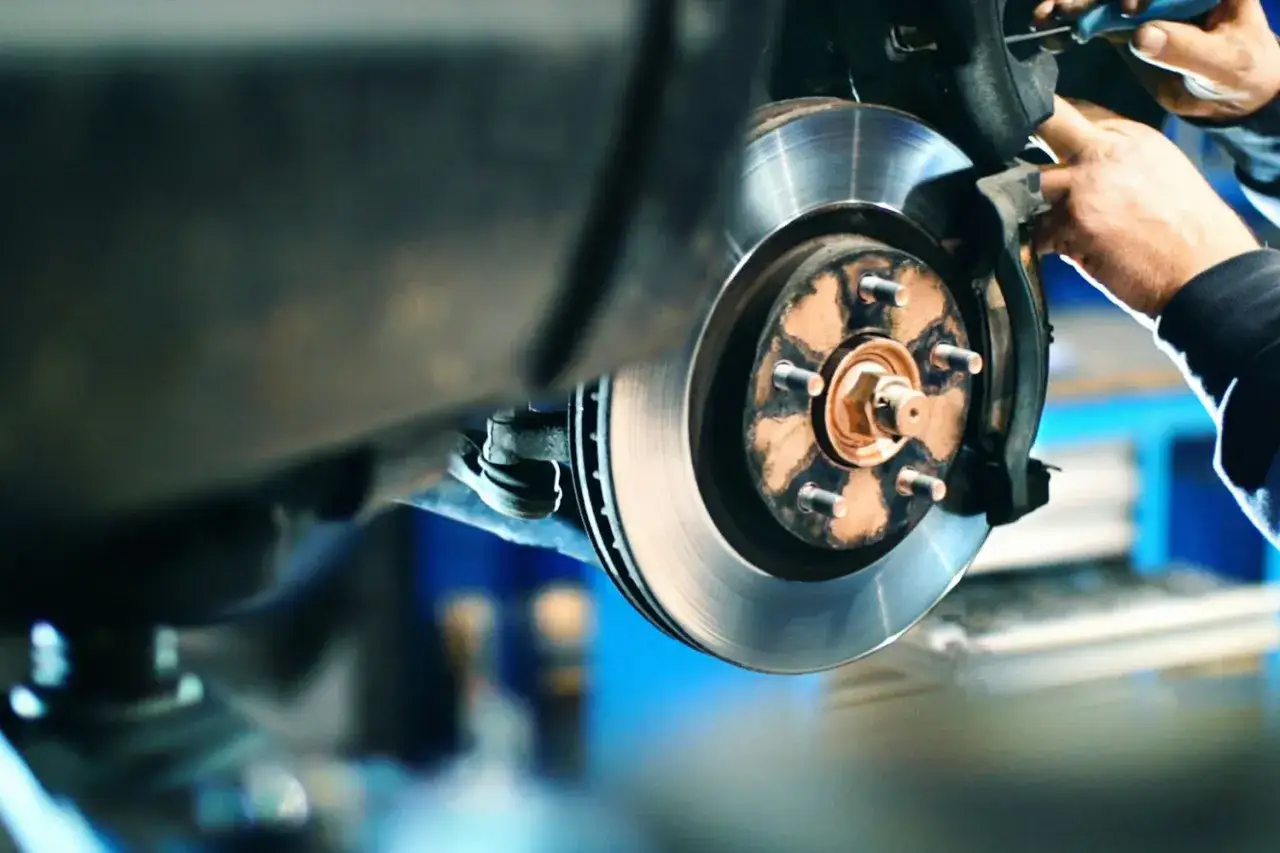 Mechanik naprawia hamulce, by wyeliminować metaliczny pisk podczas jazdy. Widoczna tarcza hamulcowa i zacisk.