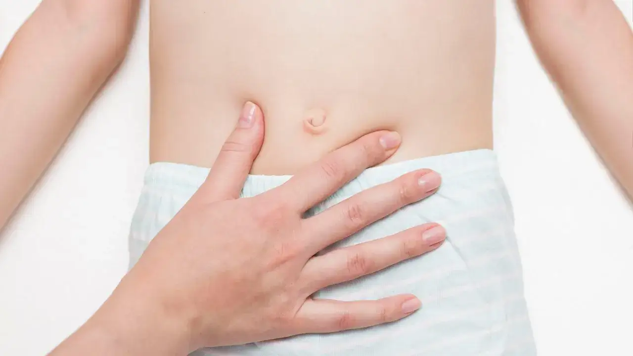 Dłoń rodzica delikatnie dotyka brzuszka dziecka, badając widoczną przepuklinę pępkową.
