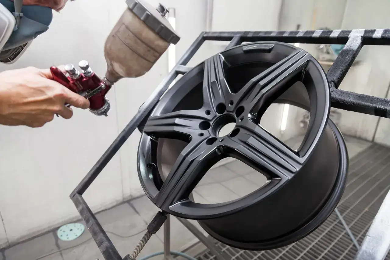 Un professionista mostra come verniciare i cerchi in lega con uno spray gun, dando un nuovo look all'auto.