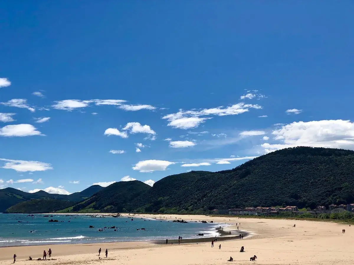 La **playa Trengandin** bajo un cielo azul con nubes blancas. Montañas verdes cubren el horizonte. Gente pasea por la arena dorada y el mar turquesa.