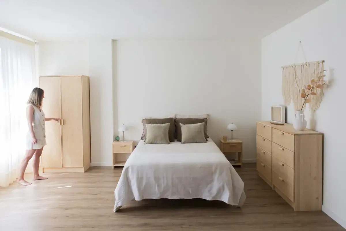 Dormitorios cálidos y acogedores con cama doble, mesitas de noche, armario de madera y cómoda. Una mujer abre el armario.