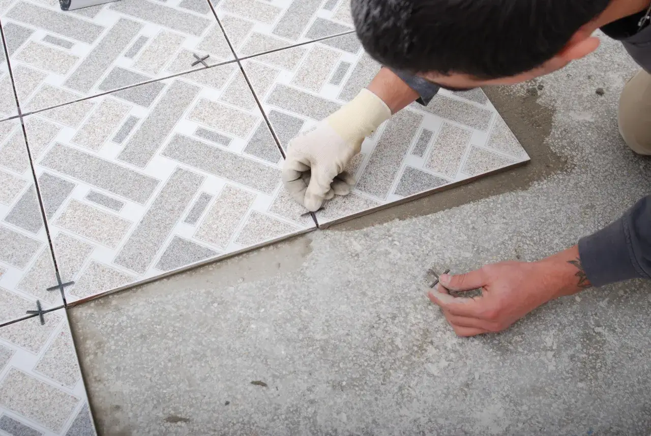 Pose d'un carrelage aux motifs g&eacute;om&eacute;triques. Un carreleur ajuste une nouvelle pi&egrave;ce, pr&eacute;parant la pose pour une d&eacute;cennale carrelage impeccable.