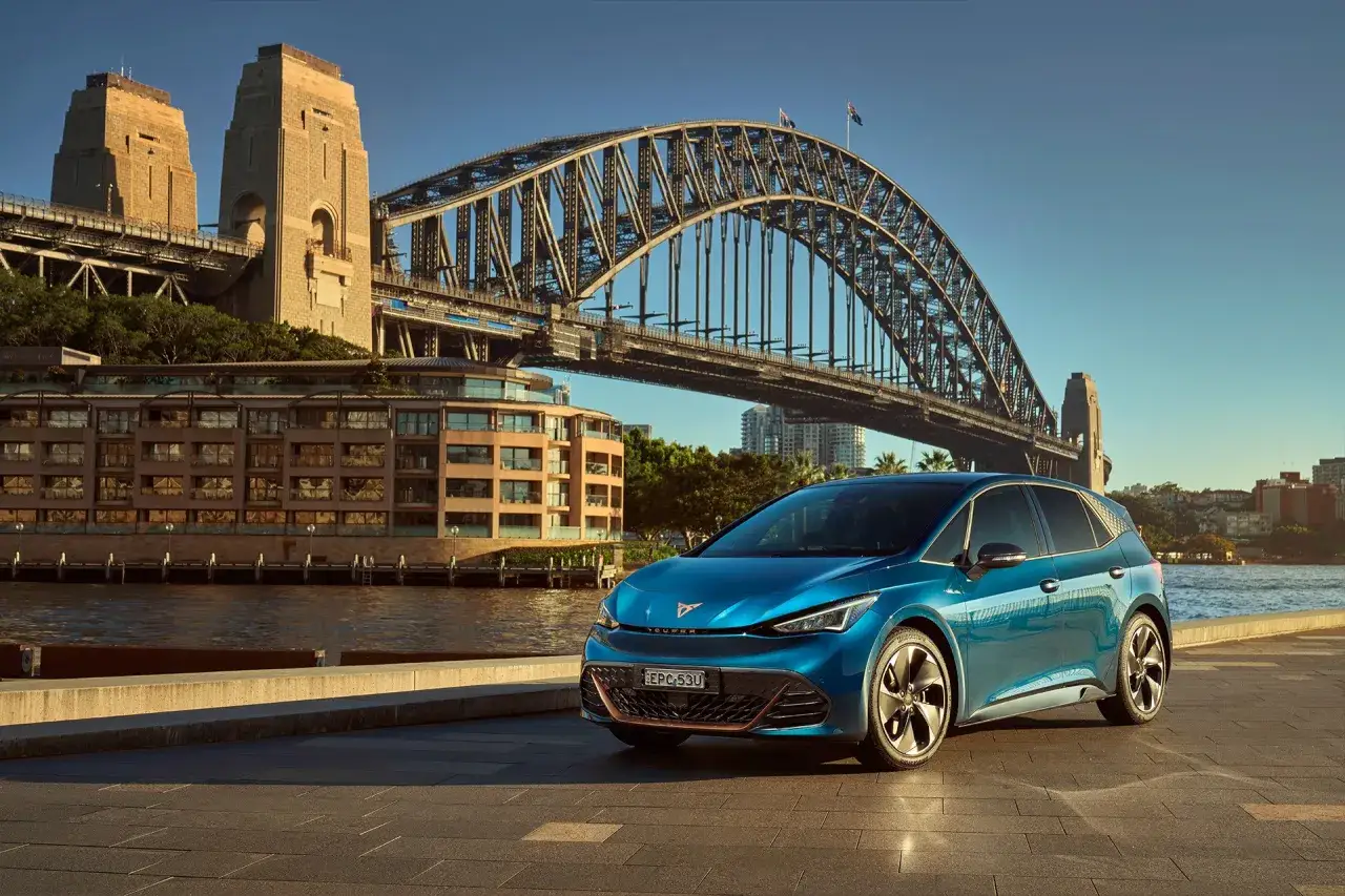 Niebieskie auto do miasta zaparkowane przy nabrzeżu w Sydney, z mostem Harbour Bridge w tle.