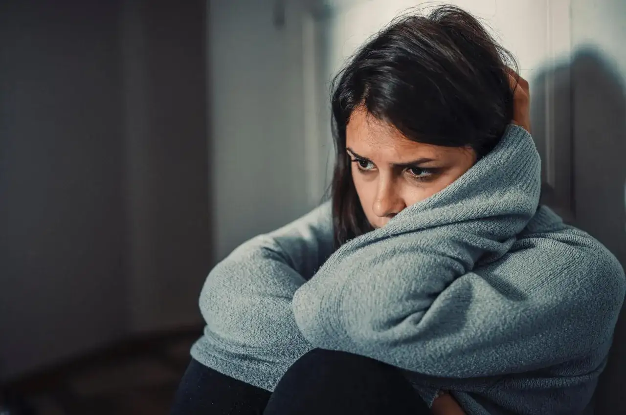 Femme seule, le regard perdu, recroquevillée dans un pull gris. Elle semble revivre les tourments d'une relation malsaine avec son ex.