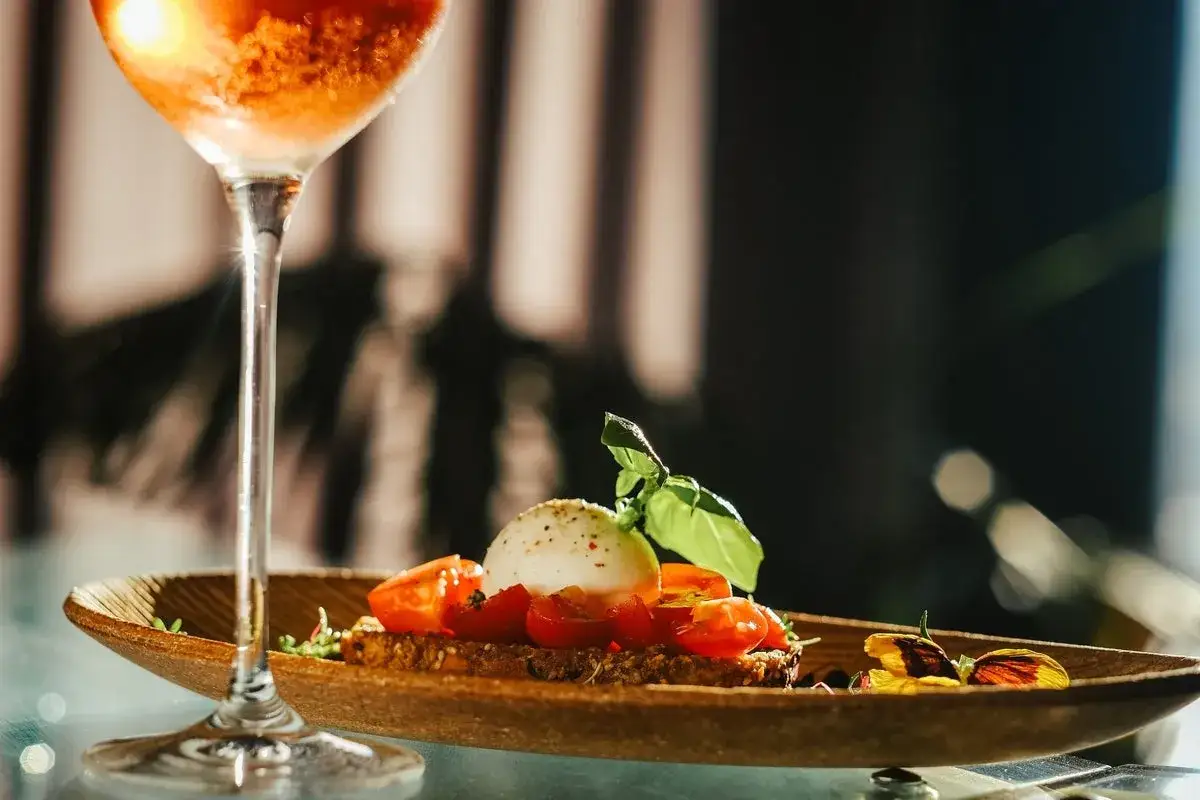 Un bicchiere di spritz alcolico accanto a un crostino con burrata, pomodorini e basilico.