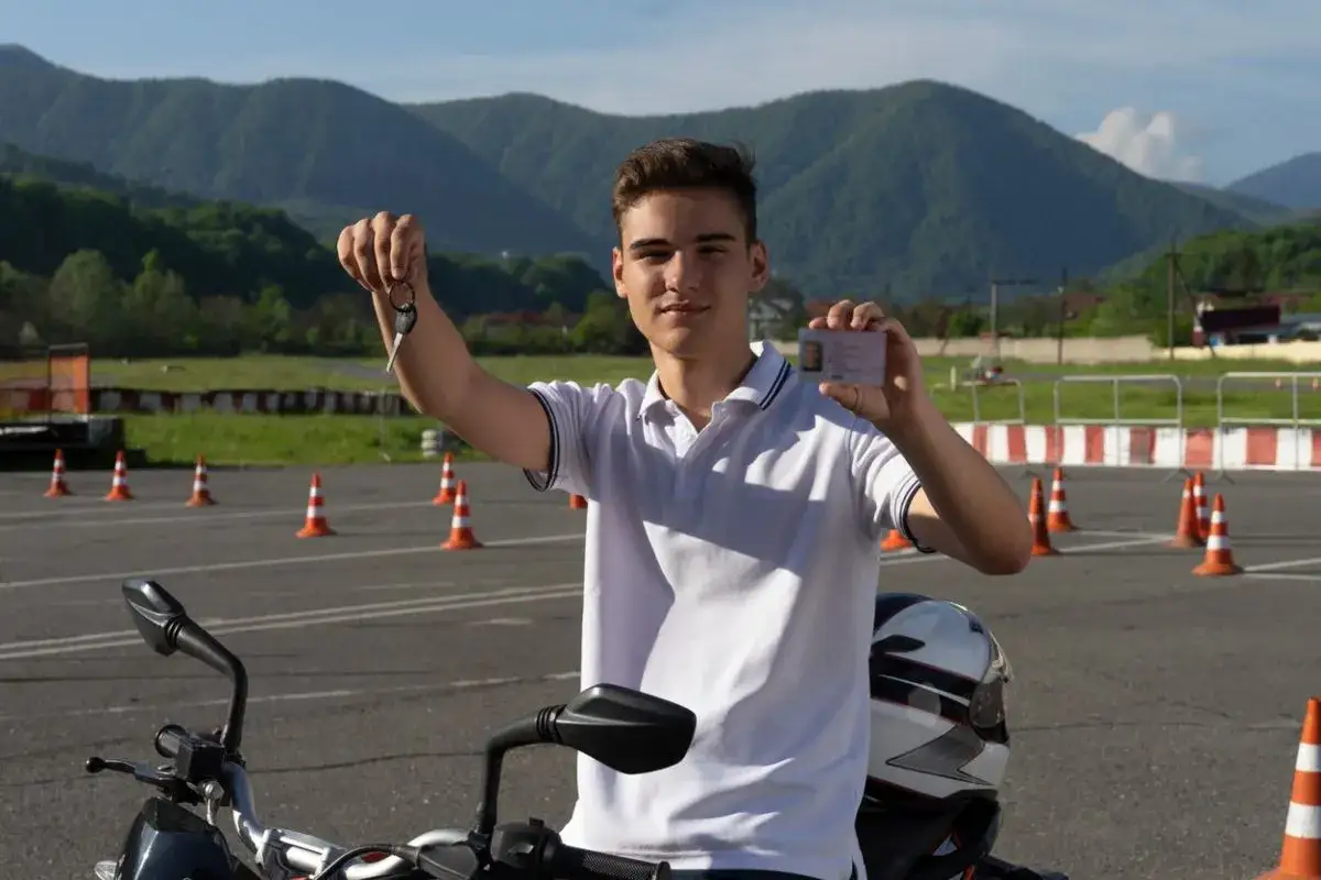 Joven sonriente muestra su carnet A1 y llaves de moto en una pista de prácticas.
