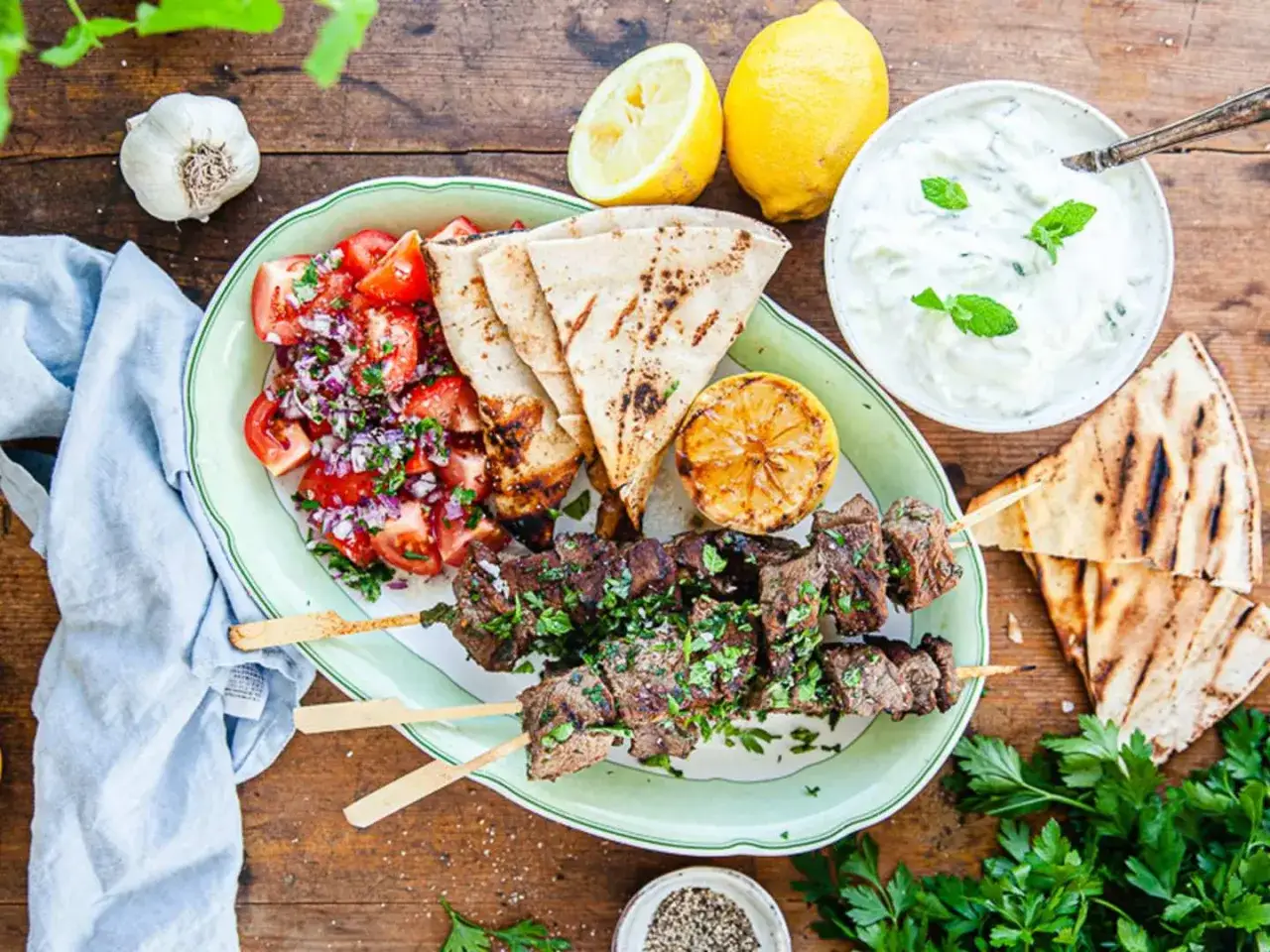 Grillspett med lamm, tomatsallad, pitabröd och en krämig yoghurtsås till lamm. Serveras med citron och färska örter.