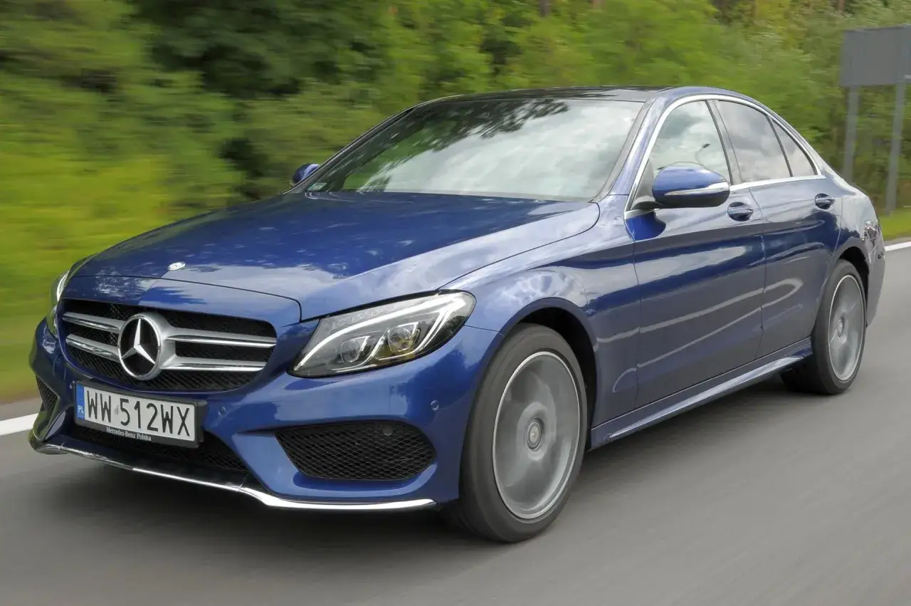 Elegancki, granatowy Mercedes-Benz Klasa C pędzi po drodze, otoczony zielenią.