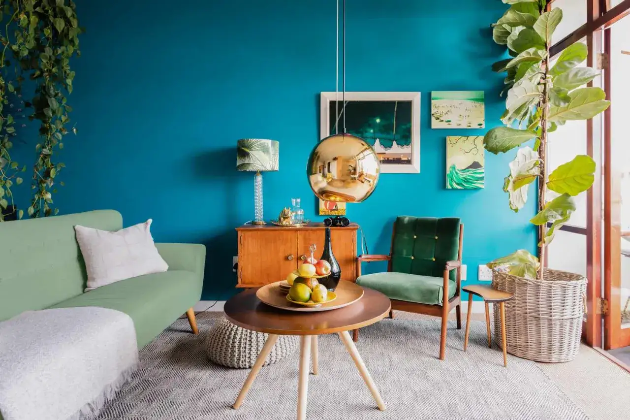 Ideas de colores para pintar un sal&oacute;n: pared azul turquesa vibrante, sof&aacute; verde menta, sill&oacute;n verde esmeralda, detalles dorados y madera.