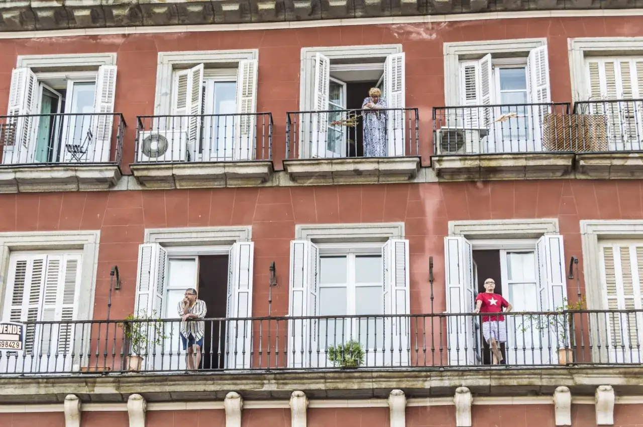 Personas en balcones de edificio con fachada rojiza, un recordatorio de la **ley de propiedad horizontal** y la convivencia vecinal.