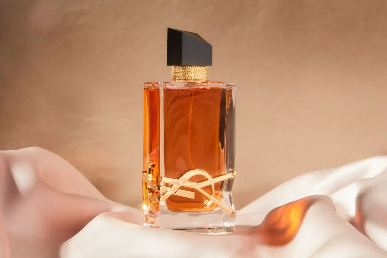 Elegancka butelka perfum Lattafa Khamrah na tle satynowych tkanin. Złote logo i bursztynowy płyn emanują luksusem.