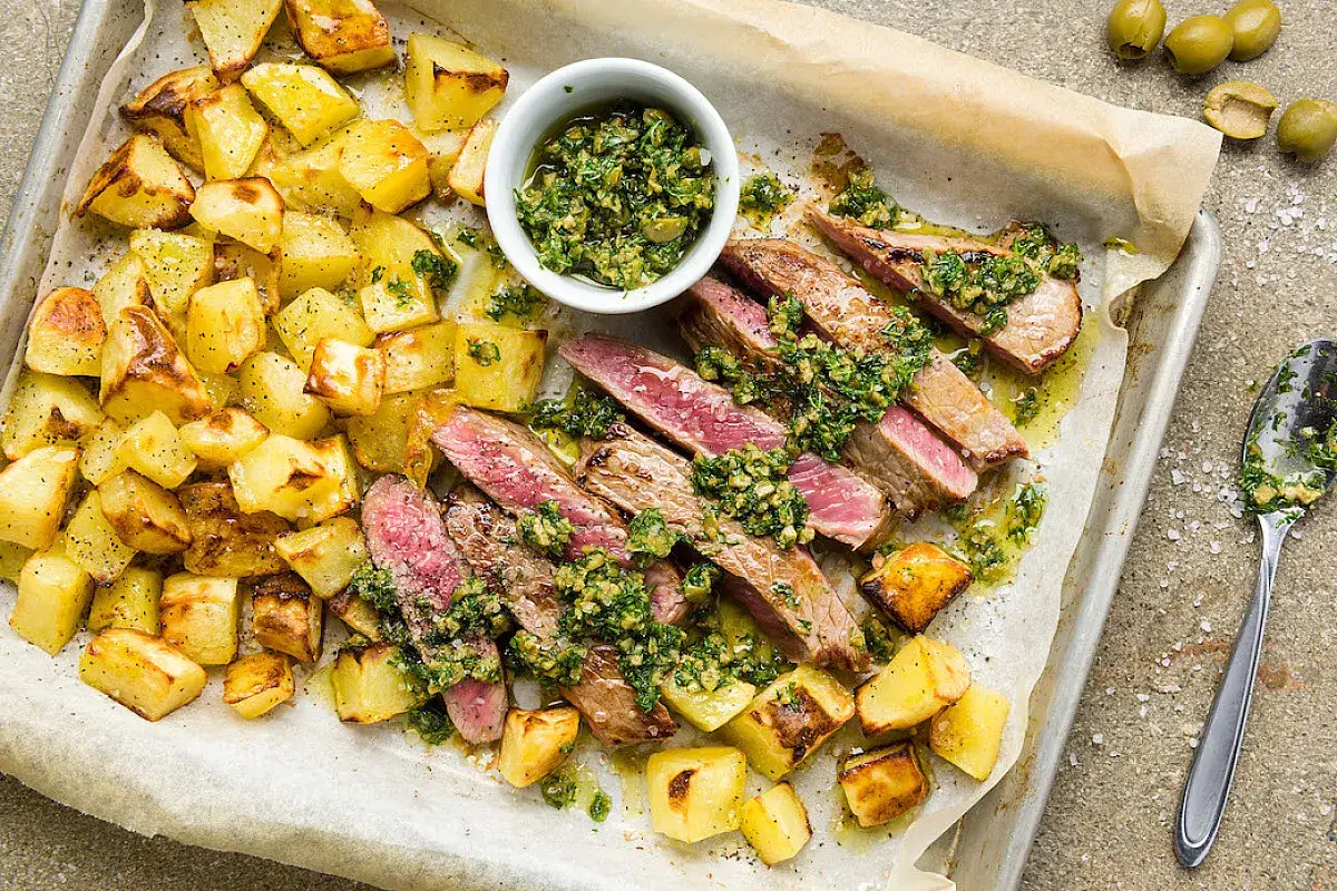 Tagliata di scottona succulenta con patate arrosto e salsa verde, un piatto invitante pronto per essere gustato.