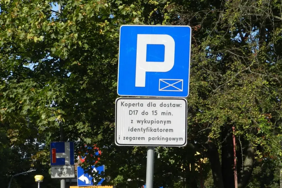 Znak informuje o kopercie dla dostaw, umożliwiającej parkowanie samochodów dostawczych na osiedlu do 15 minut z identyfikatorem i zegarem parkingowym.