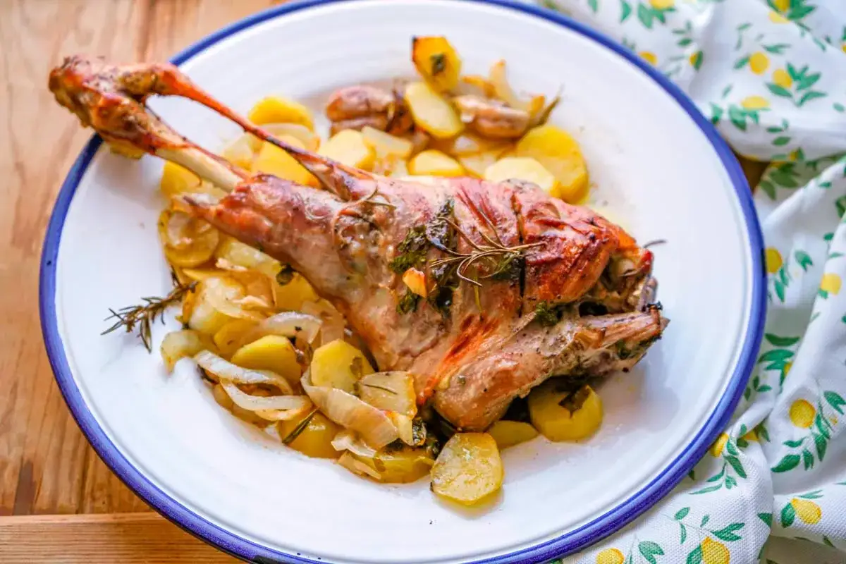 Paletilla de cordero al horno, dorada y jugosa, acompañada de patatas y cebolla asadas con romero. Un plato principal perfecto.