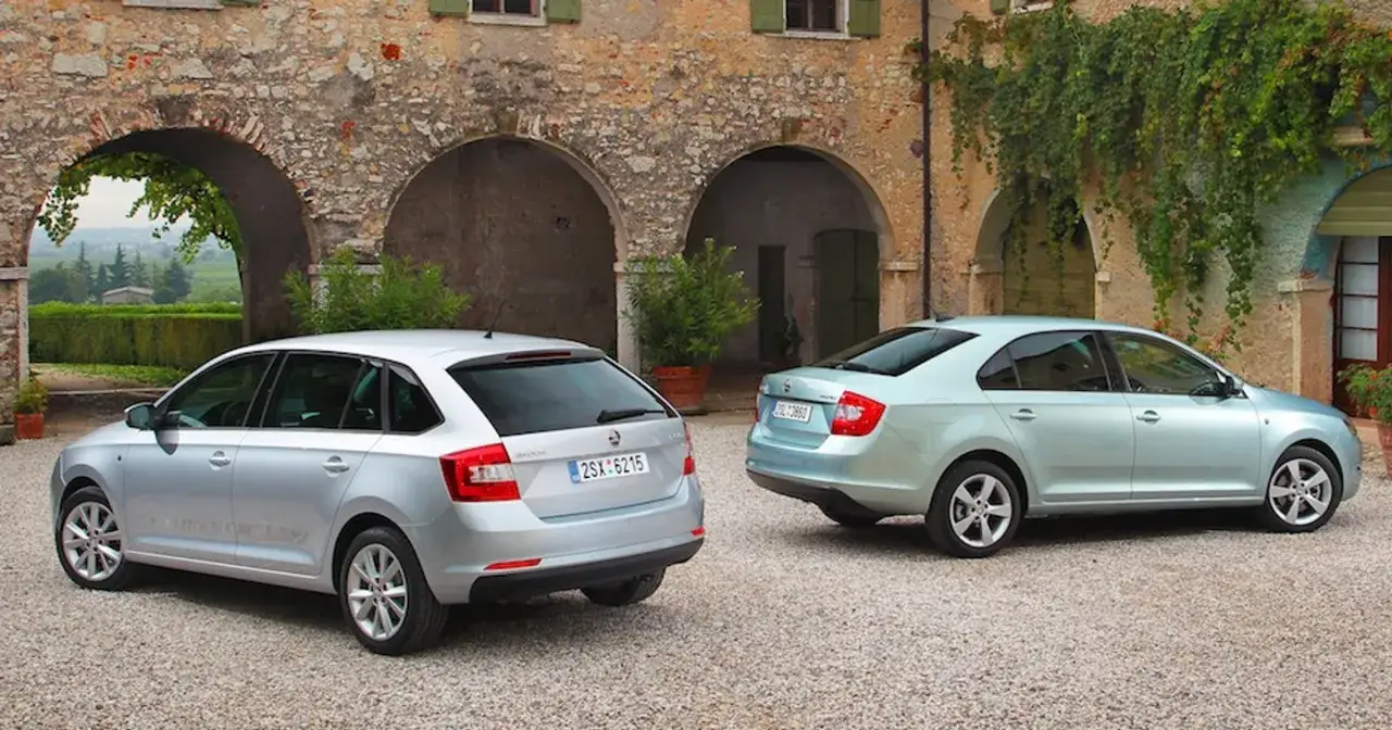 Dwa samochody Skoda Rapid: srebrny liftback i jasnoniebieski sedan, stoją przed kamiennym budynkiem z łukami.