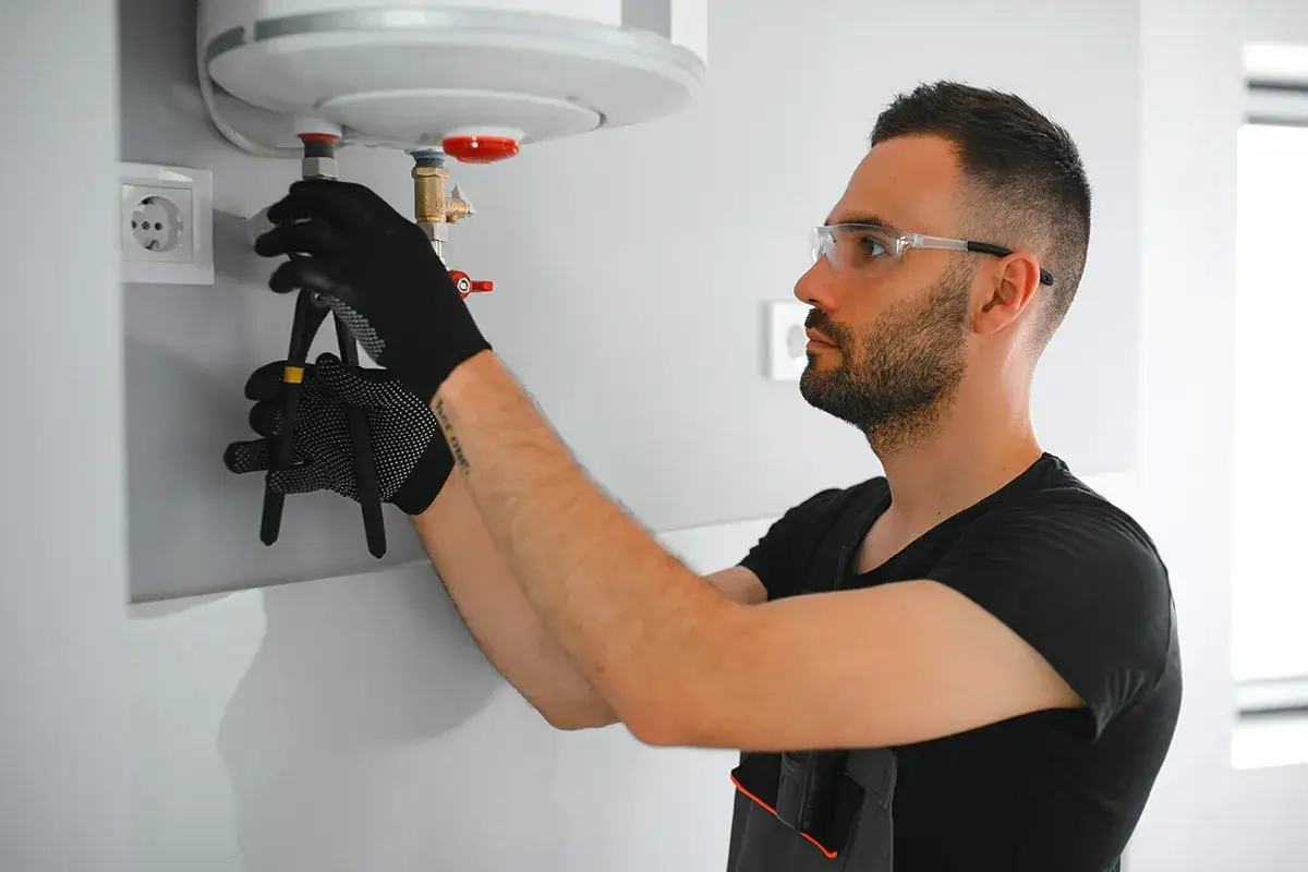 Un tecnico con occhiali protettivi controlla un boiler, forse per capire perch&eacute; i termosifoni non si scaldano.