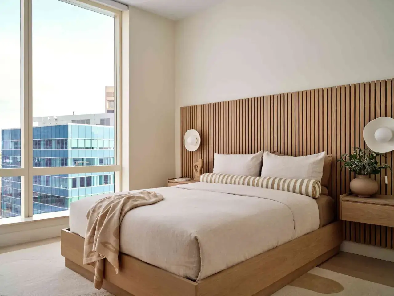 Camera da letto in stile giapponese con testiera in legno a listelli, letto king-size e vista sulla città.