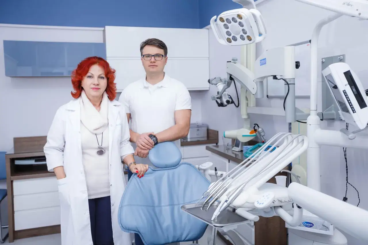 Para stomatologów w gabinecie dentystycznym, z fotelem i sprzętem.