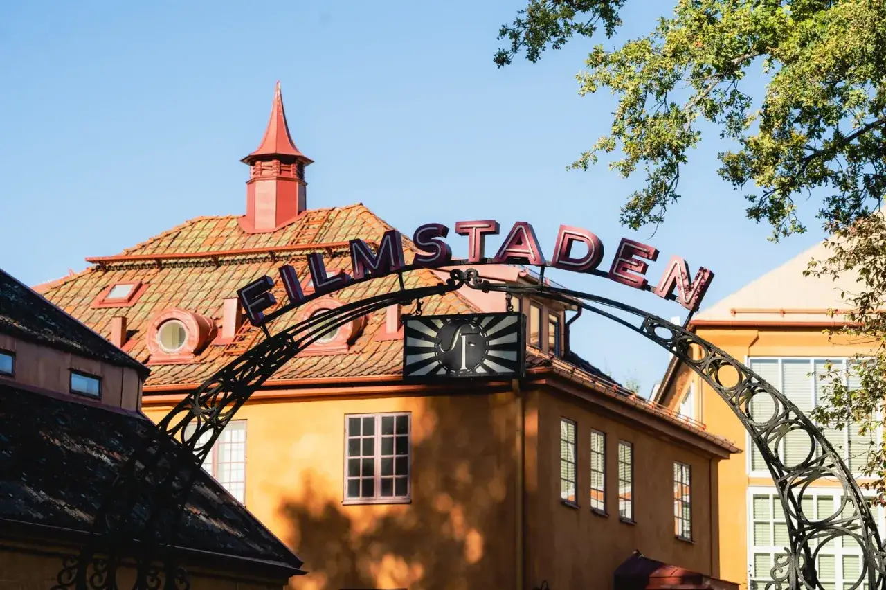 Filmstaden R&aring;sunda, med sina orangea byggnader och r&ouml;da tegeltak, v&auml;lkomnar bes&ouml;kare under en vacker sommardag.