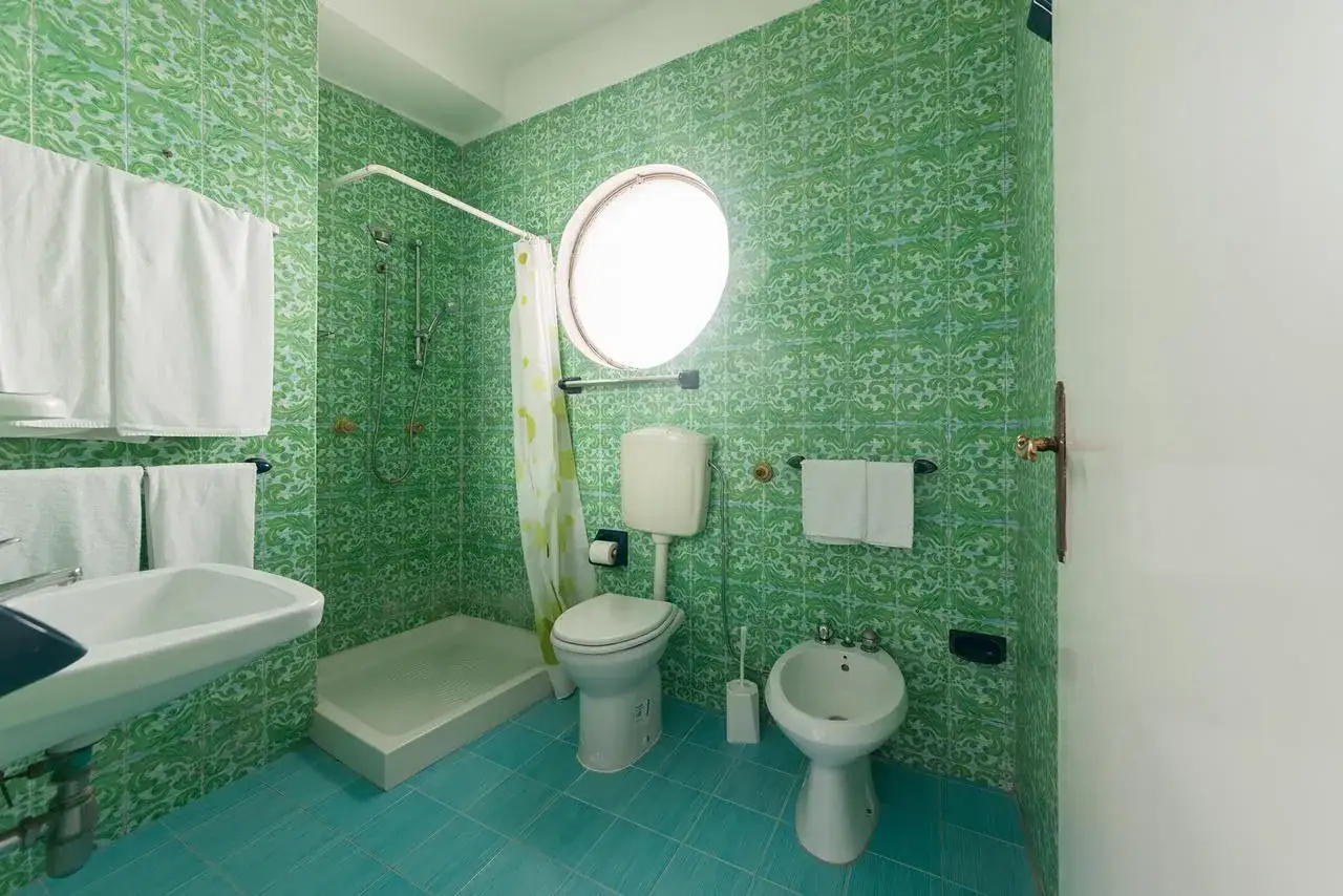 Bagno colorato con piastrelle verdi e pavimento turchese. Doccia, WC, bidet e lavandino. Un assaggio del **hotel Antonella Ischia**.