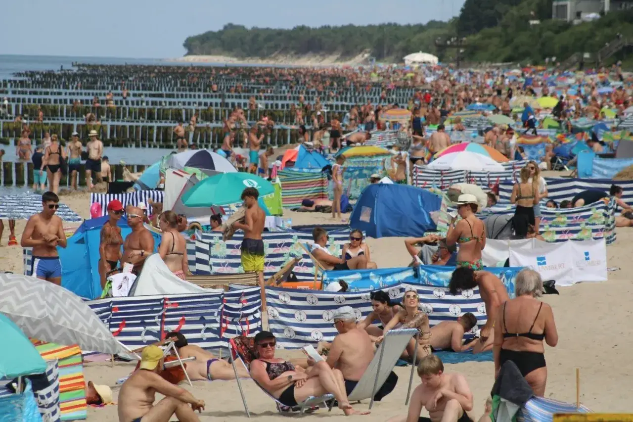Tłok na plaży w Ustroniu Morskim. Ludzie opalają się, odpoczywają pod parawanami i w namiotach.
