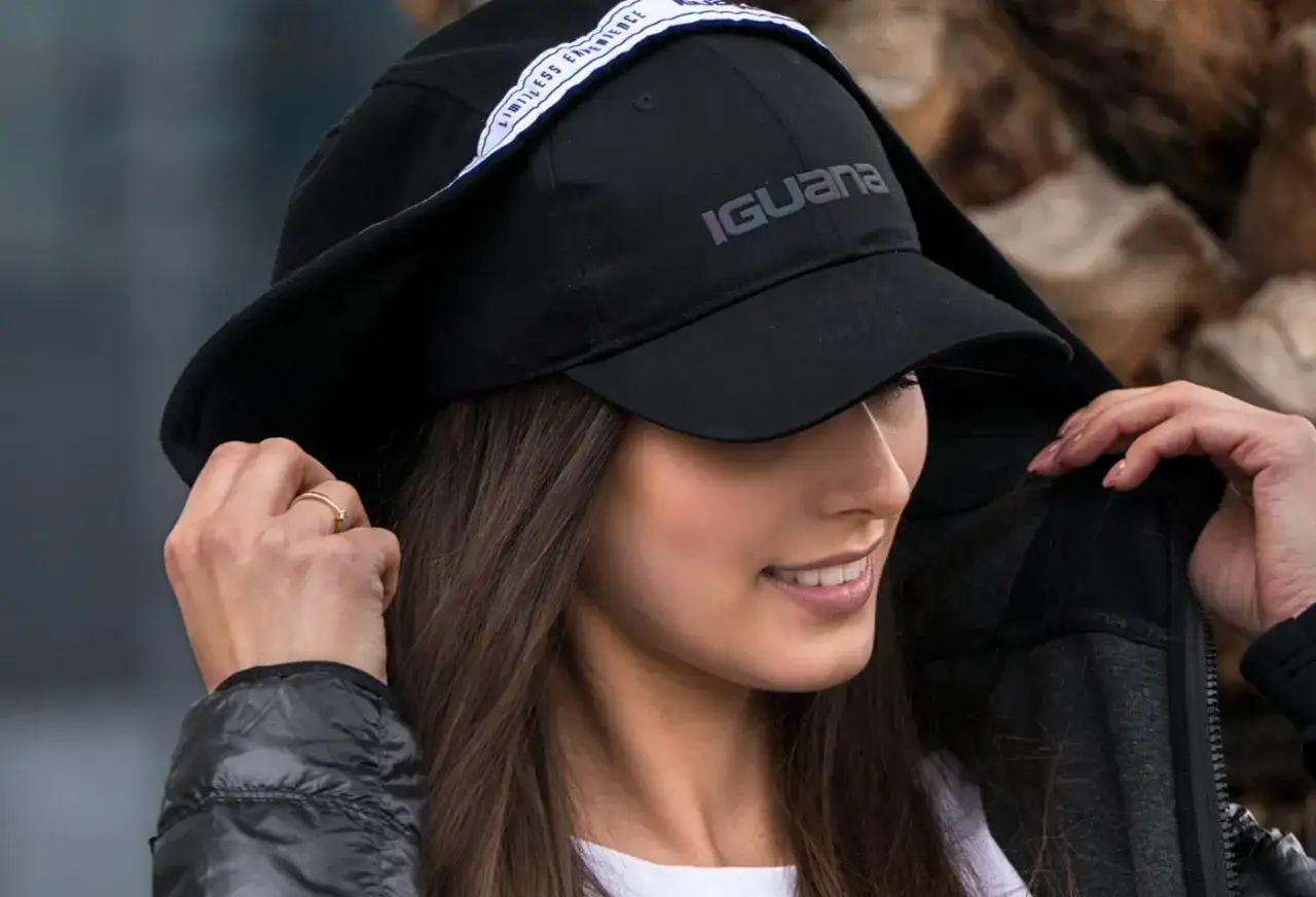 Kobieta w czarnej czapce z daszkiem z logo Iguana i białym napisem. Różne rodzaje czapek z daszkiem, jak ta, świetnie uzupełniają stylizacje.