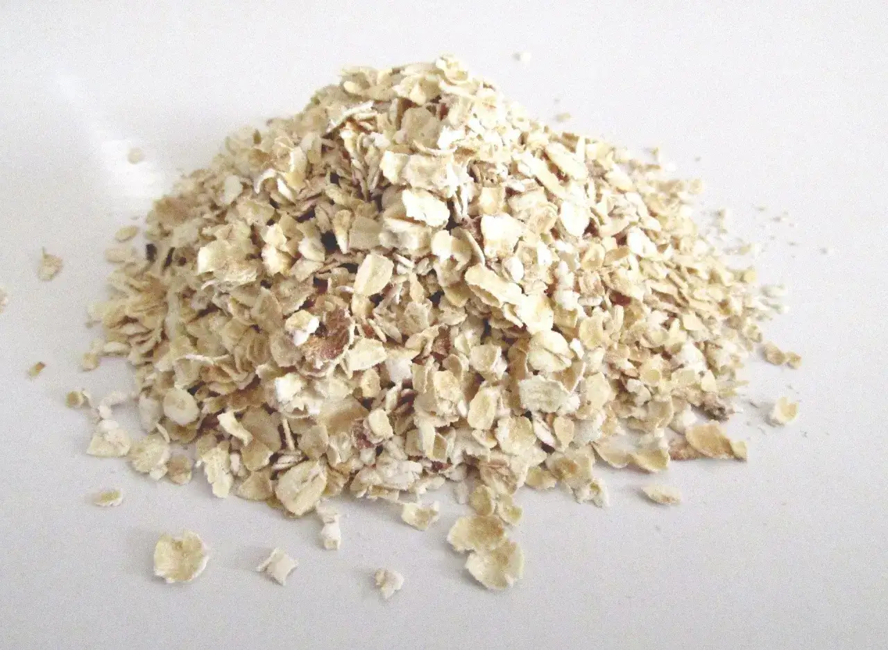 Montón de copos de avena sobre fondo blanco. Estos copos son el resultado de procesar el grano, mostrando de donde proviene la avena.