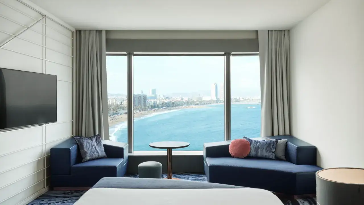 Habitación moderna con vistas al mar en el hotel W Barcelona. Sofás azules, mesa y TV.