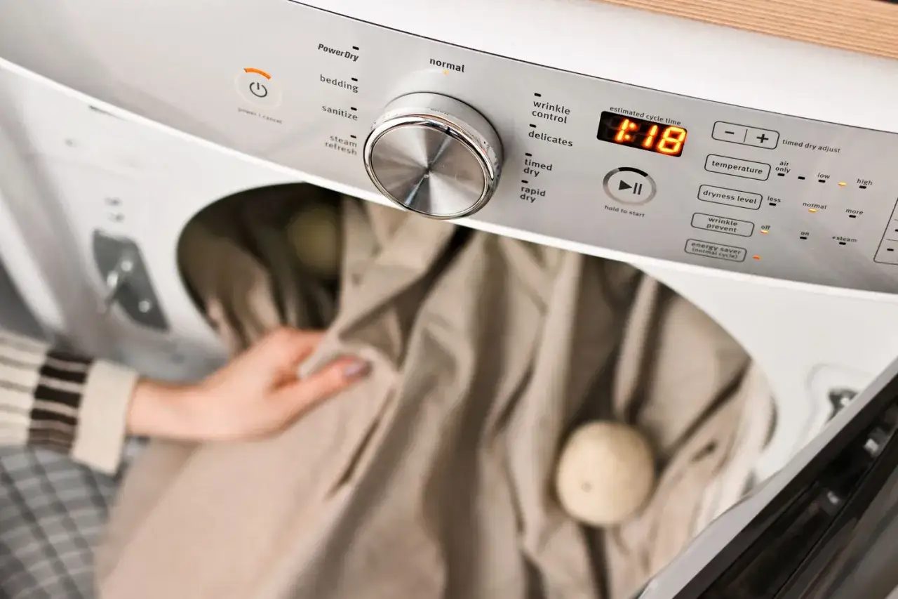 A person loads bedding into a dryer, selecting the