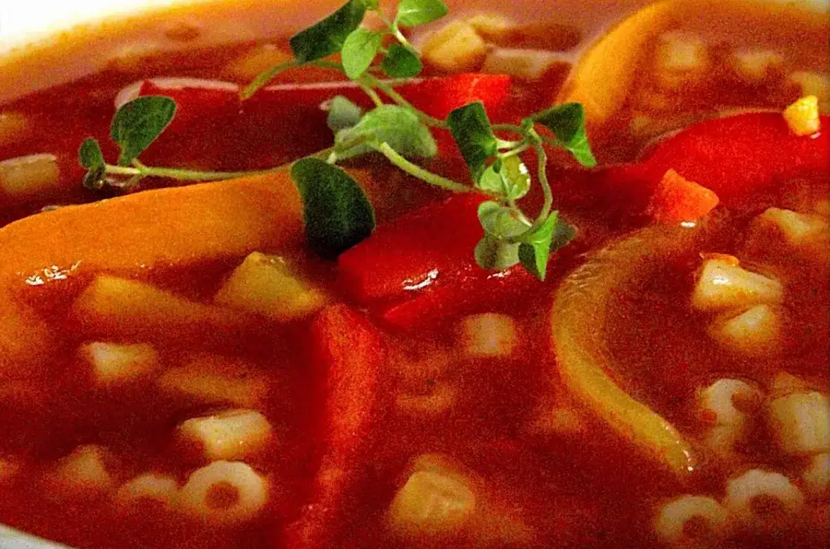 Gęsta, aromatyczna węgierska zupa paprykowa z kawałkami papryki, marchewki i makaronem w kształcie pierścieni, ozdobiona świeżymi ziołami.