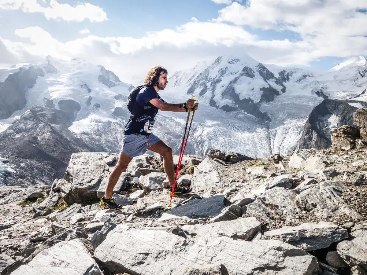 Victor Decamp Destivelle, athlète en trail, progresse sur un sentier rocheux face à des montagnes enneigées majestueuses.
