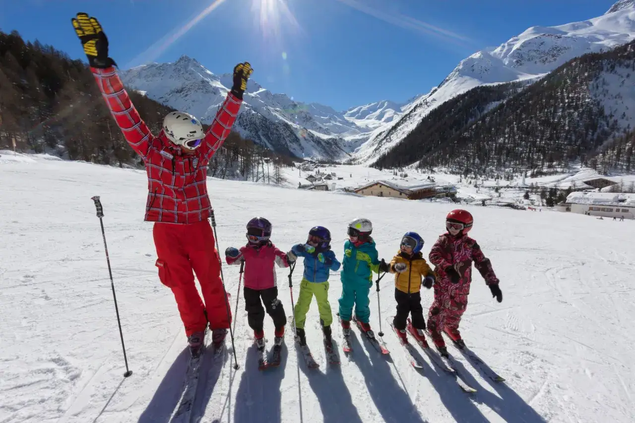 Un maestro entusiasta con bambini pronti a sciare, un luogo perfetto dove sciare con bambini, con montagne innevate e sole splendente.