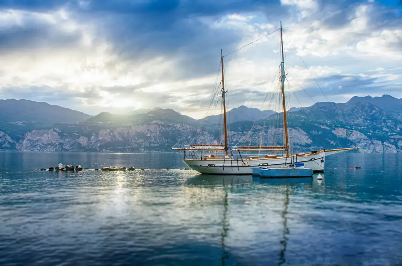 Vela bianca ormeggiata sul lago, con montagne sullo sfondo. Un'atmosfera serena a Garda citt&agrave;.