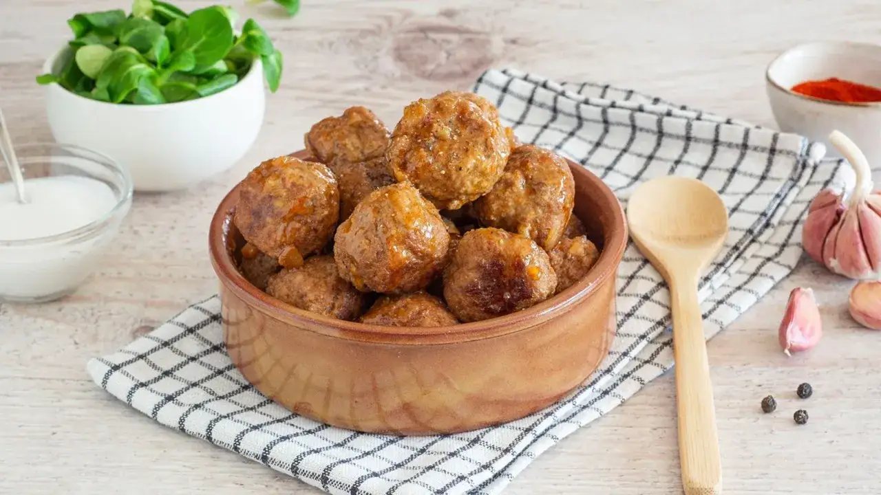 Polpette senza uova dorate e succulente in una ciotola di terracotta, accompagnate da insalata fresca, salsa e spezie.