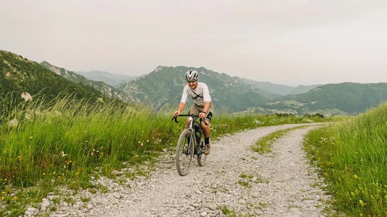 Kolarz na rowerze gravel pokonuje kamienistą ścieżkę wśród zielonych wzgórz.