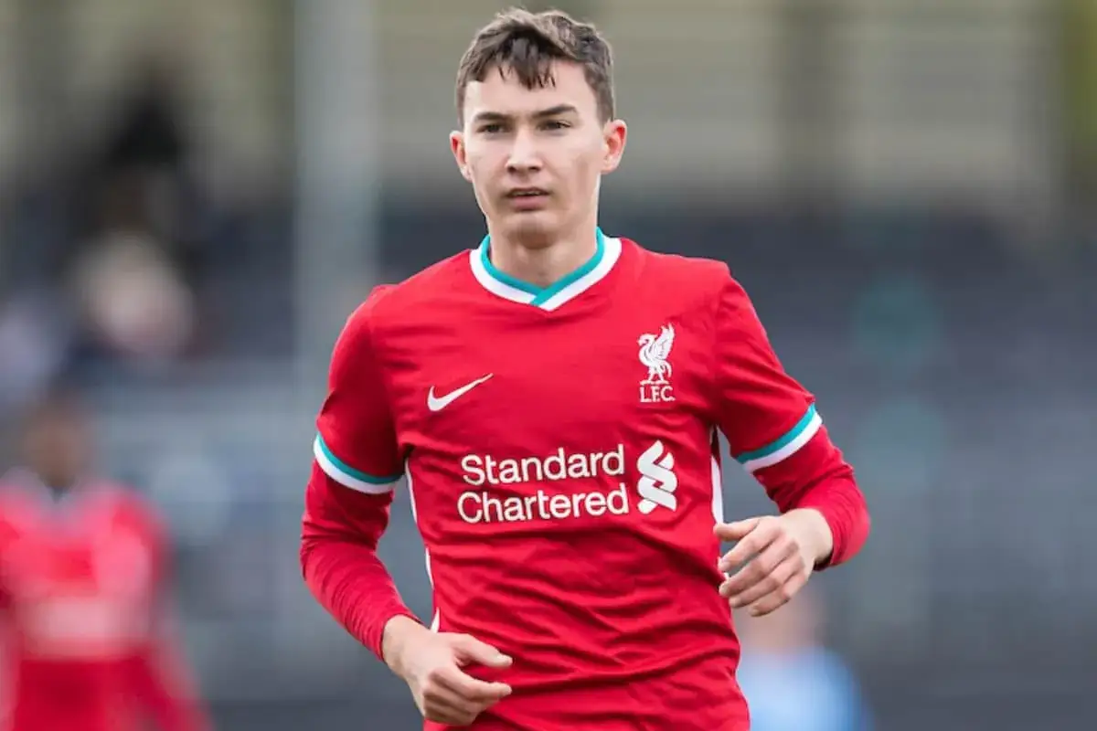Młody piłkarz Mateusz Musiałowski w czerwonej koszulce Liverpoolu, z dumą prezentuje herb klubu.