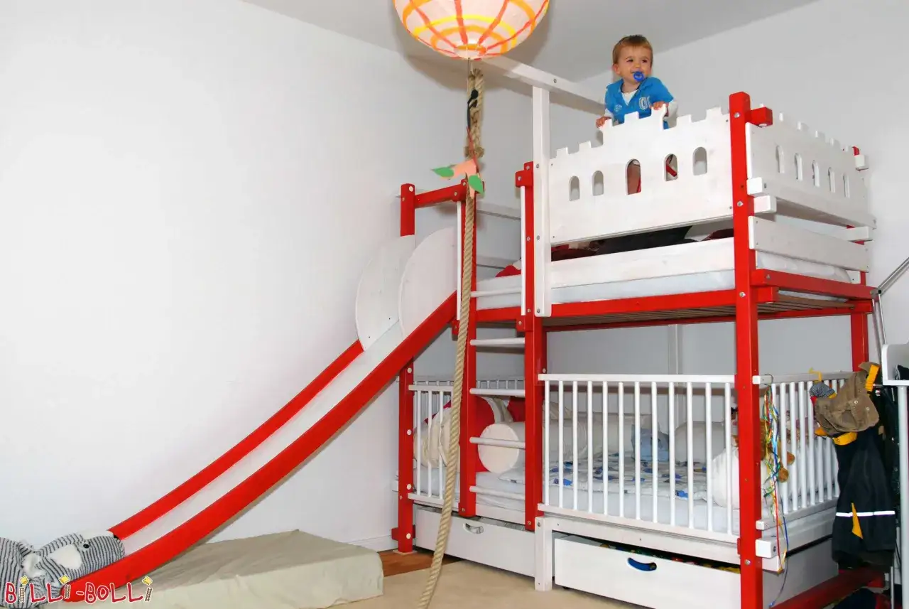 Un bimbo sorride in cima a un letto a castello con scivolo e scaletta, perfetto per avventure da che età in poi!