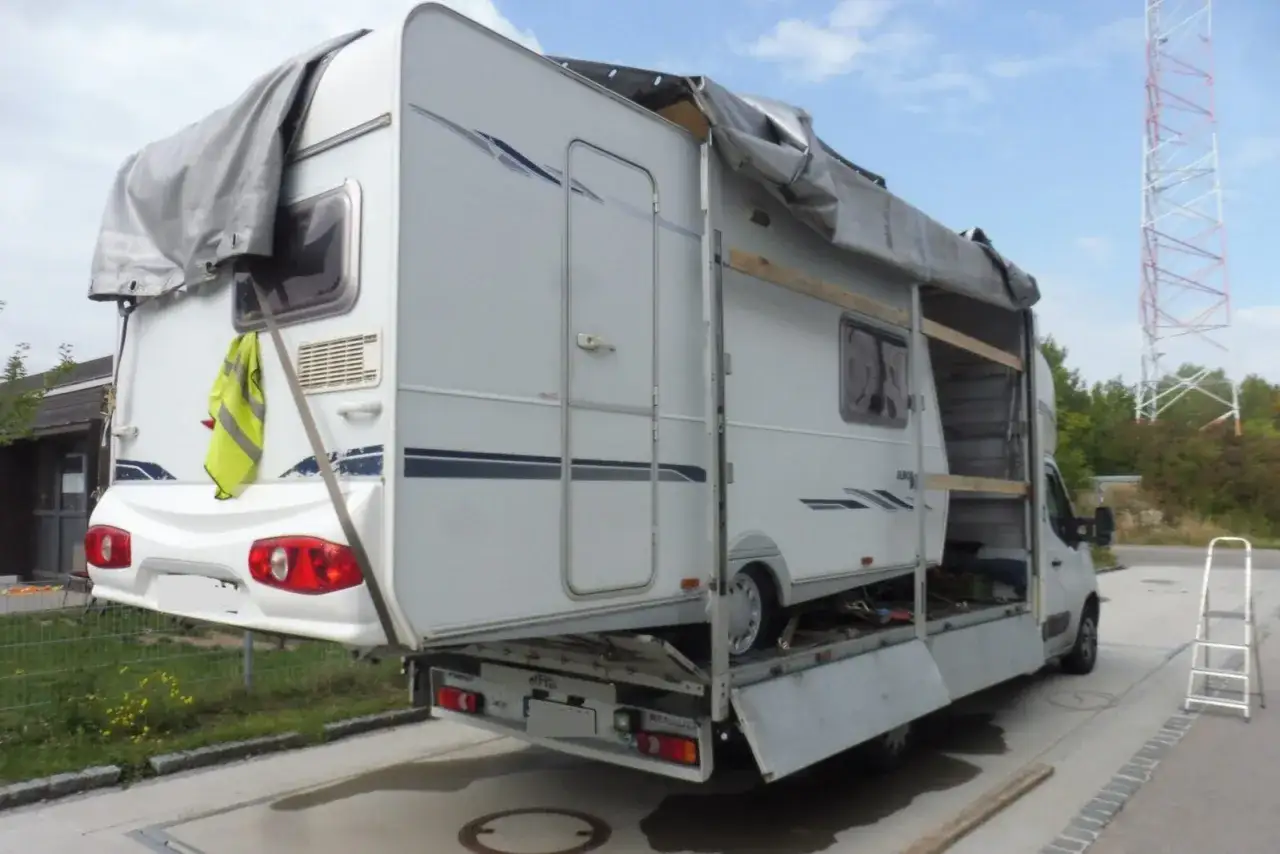 Przyczepa kempingowa transportowana na lawecie, zabezpieczona plandeką. Gotowa do podróży z prędkością 100 km/h.