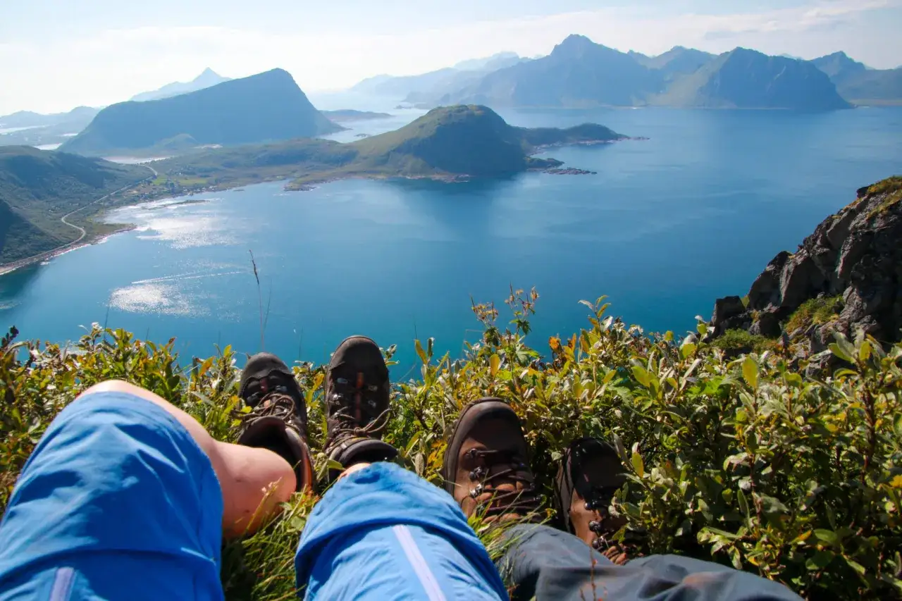 F&ouml;tter i vandringsk&auml;ngor vilar p&aring; en gr&ouml;n sluttning med en fantastisk utsikt &ouml;ver Lofoten. En perfekt dag f&ouml;r lofoten vandring.