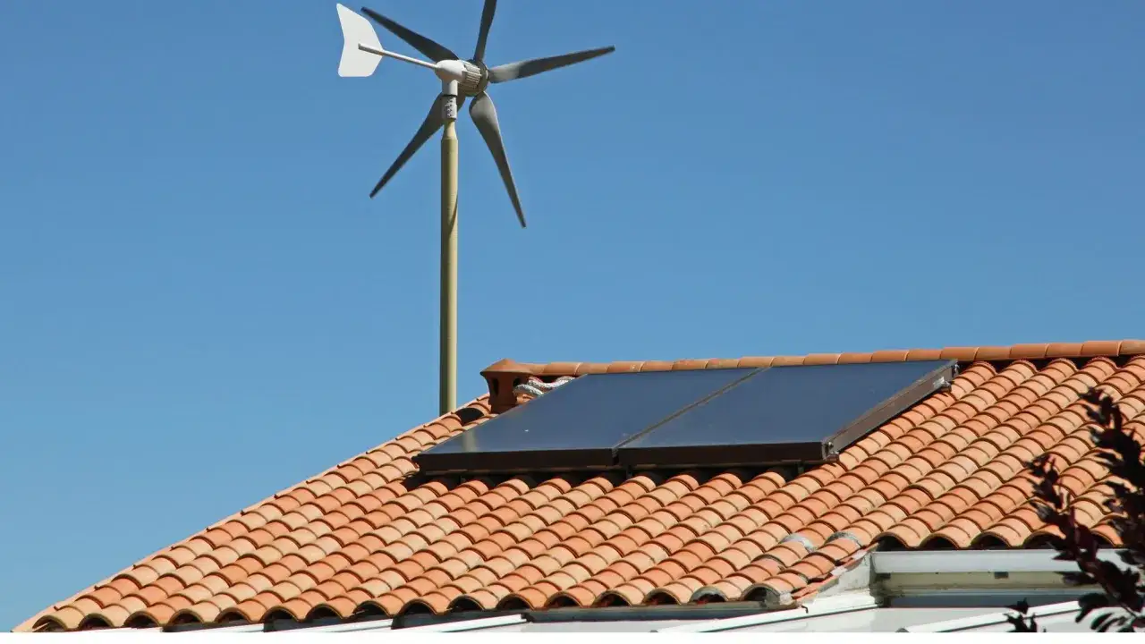 Une petite éolienne maison, avec des panneaux solaires sur un toit de tuiles rouges, sous un ciel bleu clair.